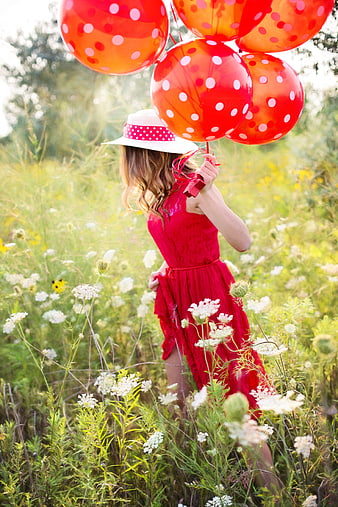 Woman in red dress holding red polka dot balloons in wildflower meadow