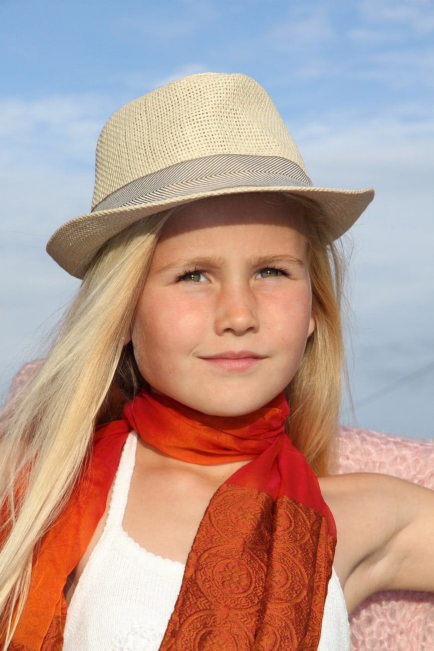 Portrait of a young blonde girl wearing a straw hat and orange scarf