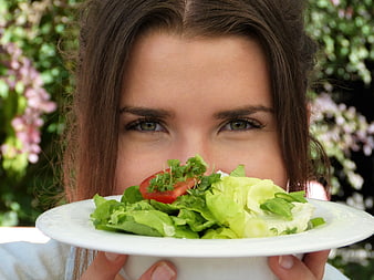 Young woman holding a fresh green salad plate in front of her face