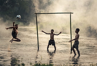 Boys playing soccer in a river with bamboo goal