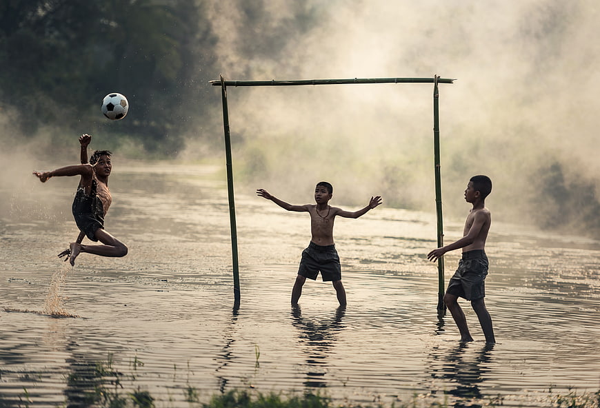 Boys playing soccer in a river with bamboo goal