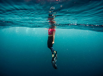 Underwater shot of woman swimming with fins in blue ocean