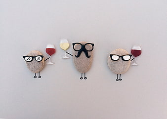 Three funny pebbles with sunglasses and wine glasses on a white background