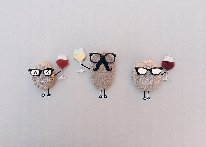 Three funny pebbles with sunglasses and wine glasses on a white background