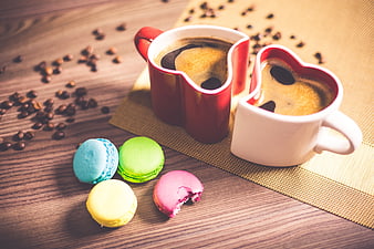 Heart-shaped coffee mugs with colorful macarons on wooden table