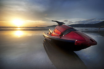 Red Jet Ski Parked on Wet Sand at Beach During Sunset