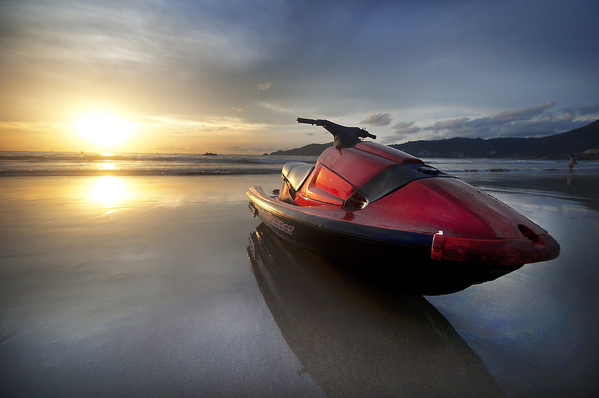 Red Jet Ski Parked on Wet Sand at Beach During Sunset