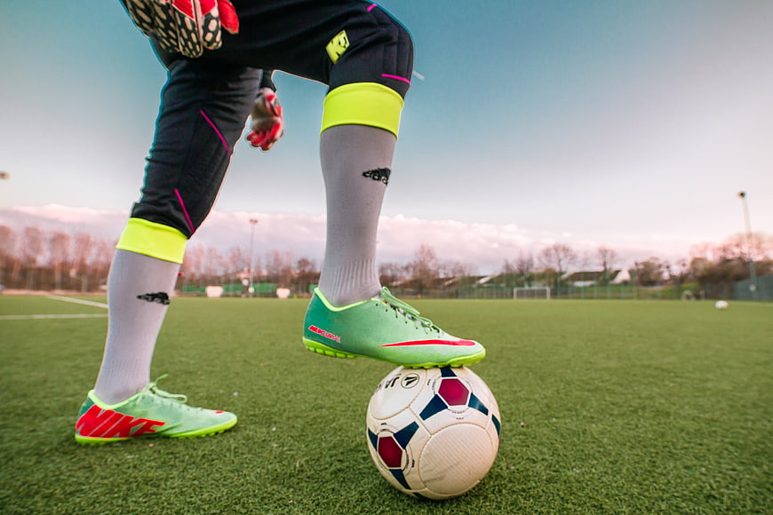 Goalkeeper with neon boots standing on soccer ball