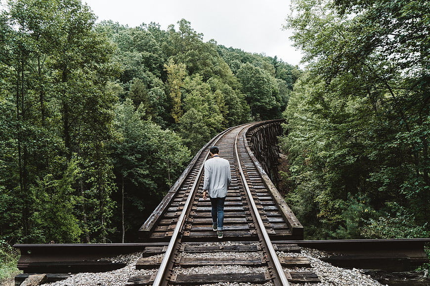 Man Walking Alone on Curved Railway Tracks in Forest