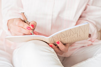 Woman writing in a beige notebook with pink nails