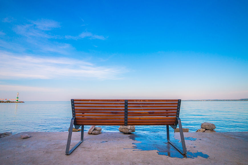 Empty wooden bench facing calm blue sea with lighthouse