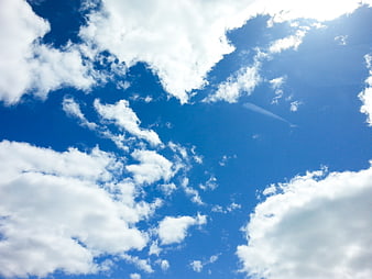 Bright blue sky with white clouds and airplane contrail