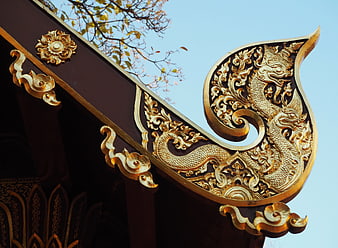 Ornate golden Thai temple roof decoration against blue sky