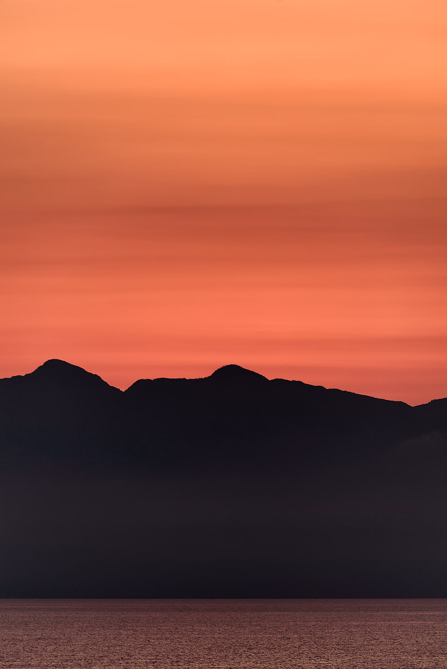 Silhouetted Mountains Against Vibrant Orange Sunset Sky