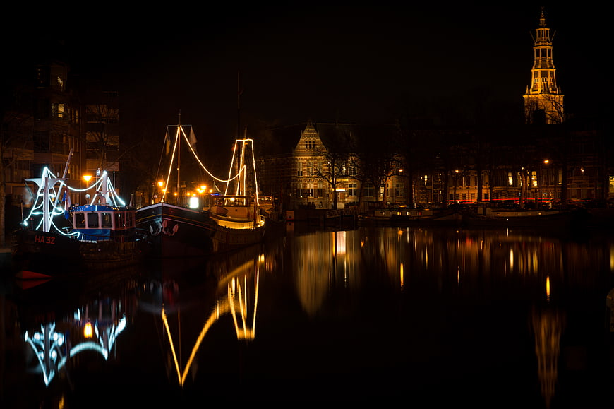 Night view of illuminated boats and church tower on a canal in Groningen, Netherlands