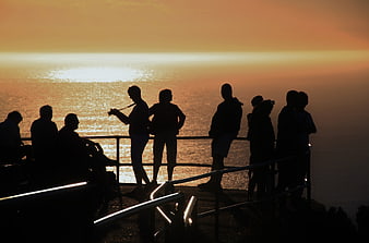 Silhouetted tourists watching sunset over the ocean from a coastal viewpoint