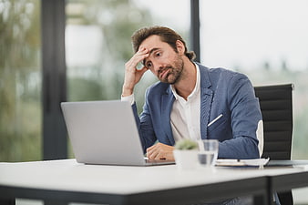 Stressed businessman holding head while working on laptop
