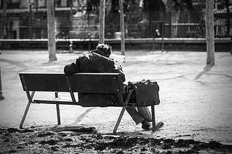 Man reading newspaper on park bench in black and white