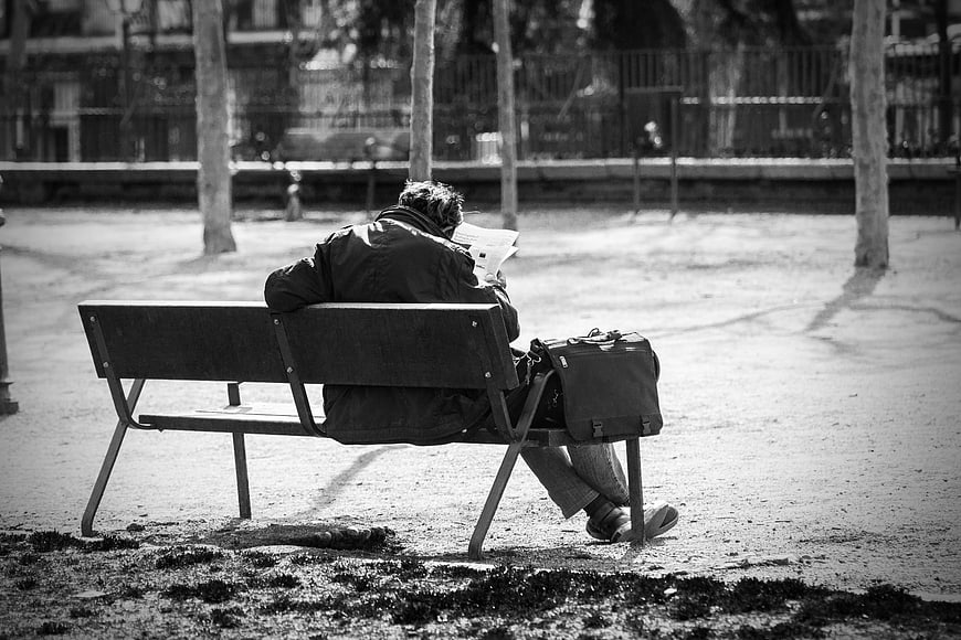 Man reading newspaper on park bench in black and white