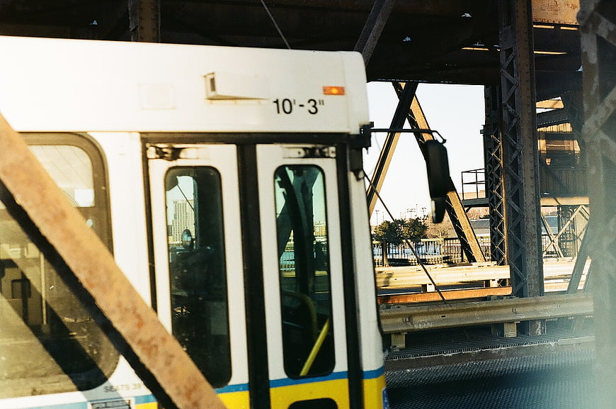 White commuter train passing under steel bridge structure