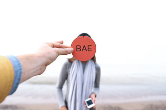 Hand holding red tag with BAE text on blurred beach background