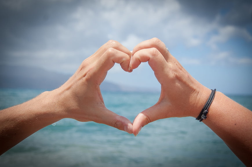Hands forming heart shape against ocean background
