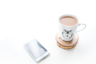 White smartphone and coffee mug with wolf design on white surface
