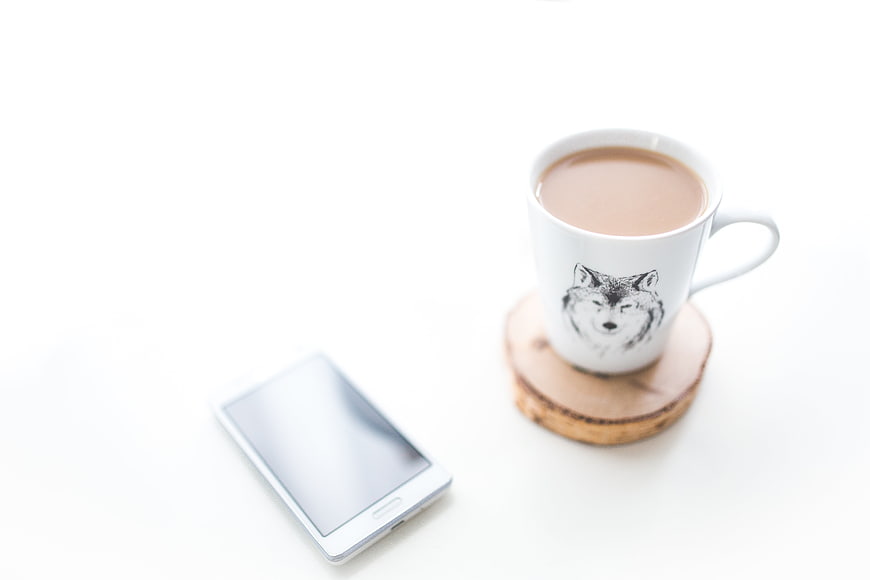 White smartphone and coffee mug with wolf design on white surface