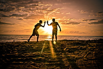 Silhouette of Two Men High-Fiving on Beach at Sunset
