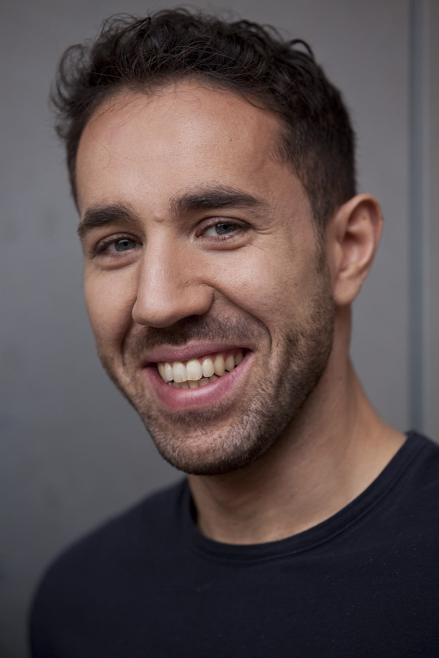 Close-up portrait of a smiling man with short dark hair and stubble