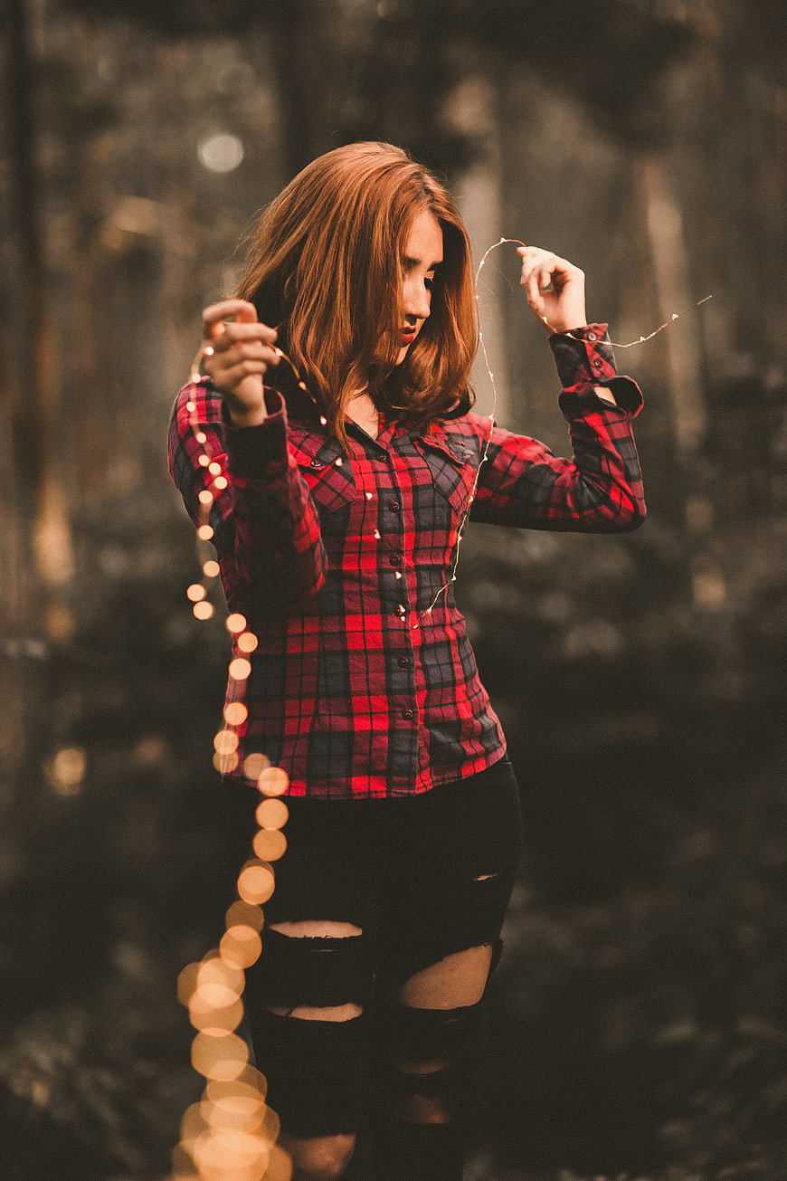 Woman in Red Plaid Shirt Holding Fairy Lights in Forest