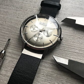 Silver O.W.I wristwatch with black leather strap on gray textured surface