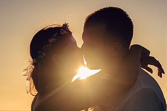 Silhouette of couple kissing at sunset with sun flare