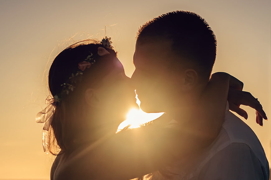 Silhouette of couple kissing at sunset with sun flare