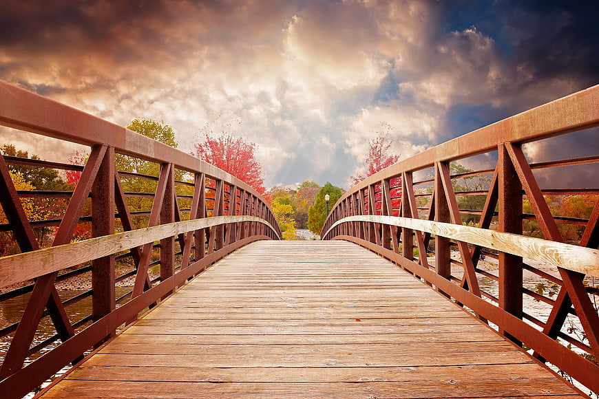 Wooden Bridge Over River in Autumn with Dramatic Sky