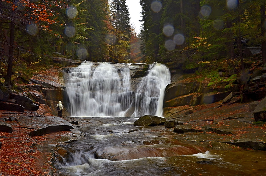 Autumn waterfall in forest with hiker and raindrops