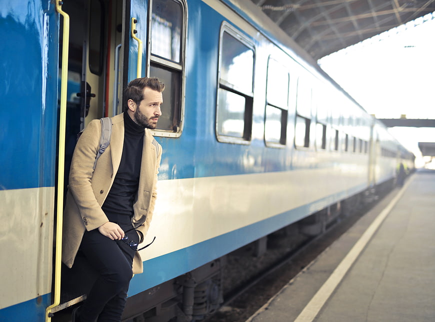 Stylish man with beard leaning out of blue train door at station