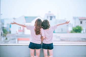 Two women with arms outstretched on a balcony