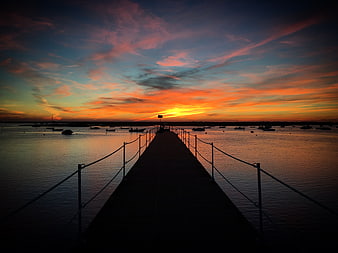 Silhouetted pier at sunset with vibrant orange and blue sky