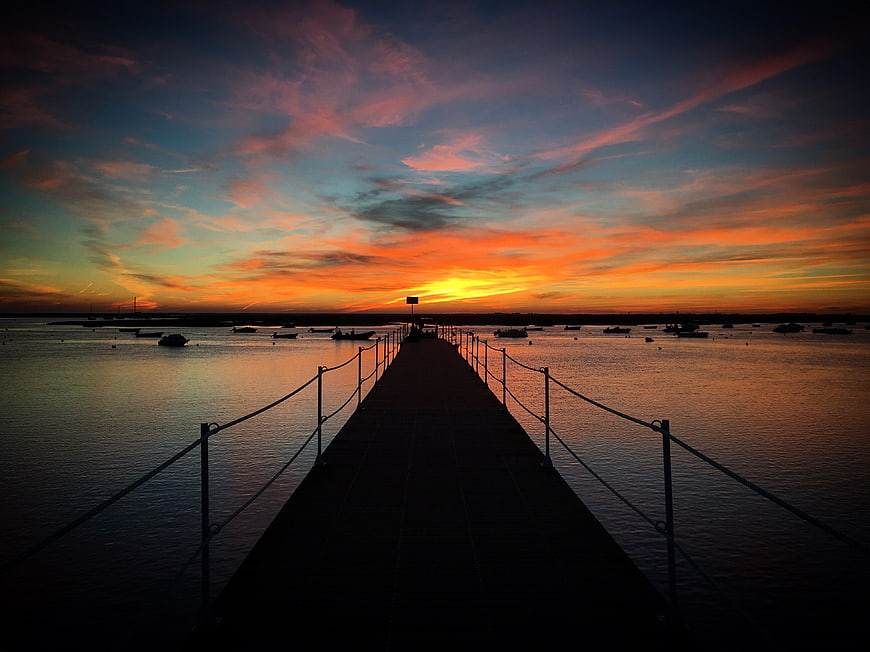 Silhouetted pier at sunset with vibrant orange and blue sky