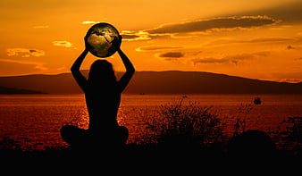 Silhouette of woman holding globe at sunset