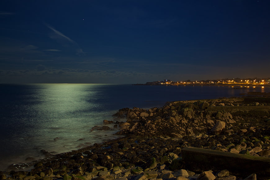 Nighttime Coastal View with Rocky Shore and Distant City Lights