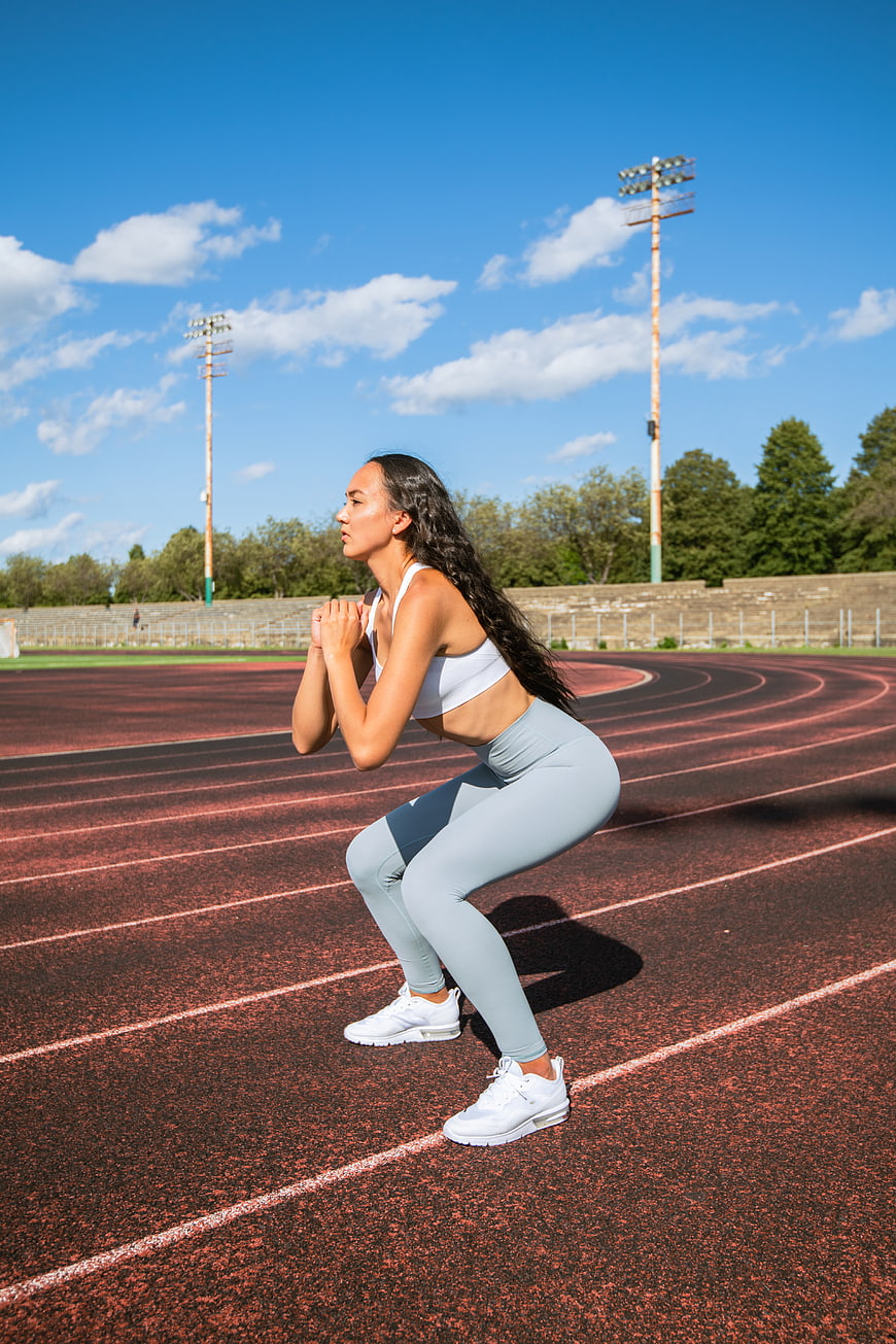 Woman performing squat exercise on outdoor running track