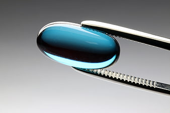 Blue Capsule Pill Held In Metal Tweezers On Gray Background
