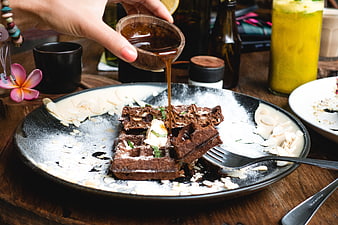 Pouring maple syrup on chocolate waffle with almond slices