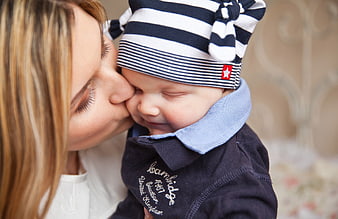 Mother kissing smiling baby wearing striped hat