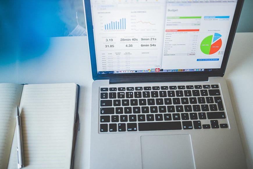 Laptop with financial charts and notebook on desk