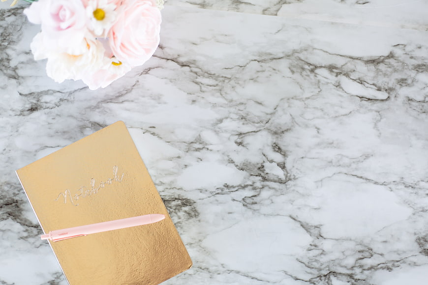 Gold Notebook and Pink Flowers on Marble Background