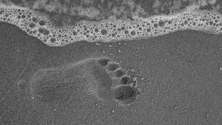 Black and white footprint in wet sand with sea foam