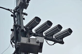 Multiple CCTV surveillance cameras mounted on a metal pole against a gray sky